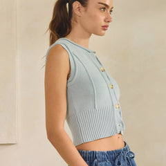 Woman wearing a light blue button down tank top with blue jeans on a beige background