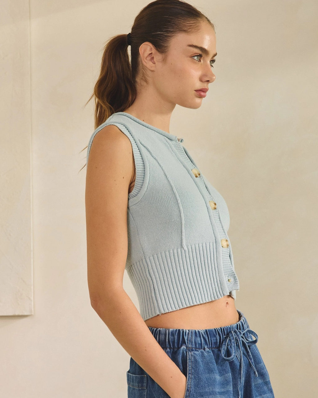 Woman wearing a light blue button down tank top with blue jeans on a beige background
