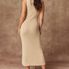 A woman wearing a sleeveless beige ribbed knit midi dress, shown from the back against a textured brown studio backdrop.