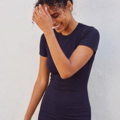 A woman wearing a dark navy blue short-sleeve bodycon dress, posing against a light-colored textured wall.