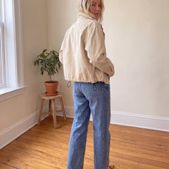 Woman wearing cream cropped canvas jacket showing relaxed back fit, back yoke and adjustable drawstring hem