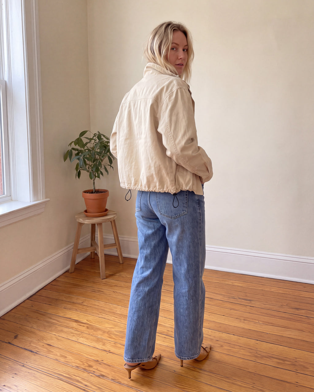 Woman wearing cream cropped canvas jacket showing relaxed back fit, back yoke and adjustable drawstring hem