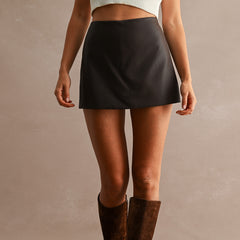 Women's dark faux leather high waist mini skort styled with a cream knit top and brown knee-high suede boots