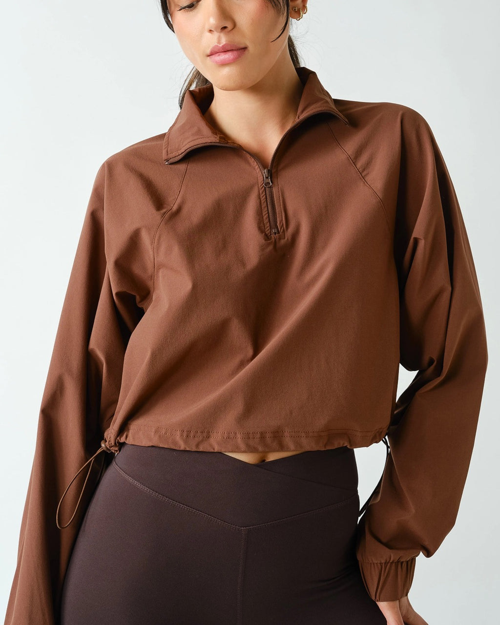 Women's chocolate brown half zip athleisure pullover with structured fit, long sleeves, four-way stretch fabric, and cropped silhouette.