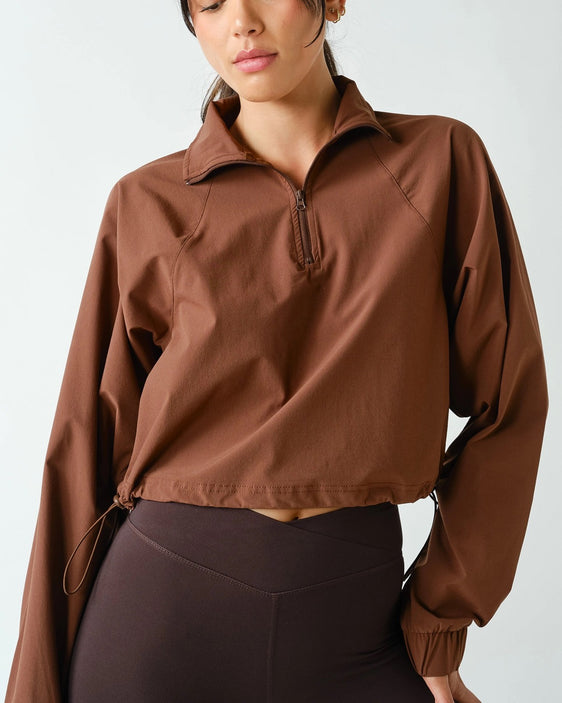 Women's chocolate brown half zip athleisure pullover with structured fit, long sleeves, four-way stretch fabric, and cropped silhouette.
