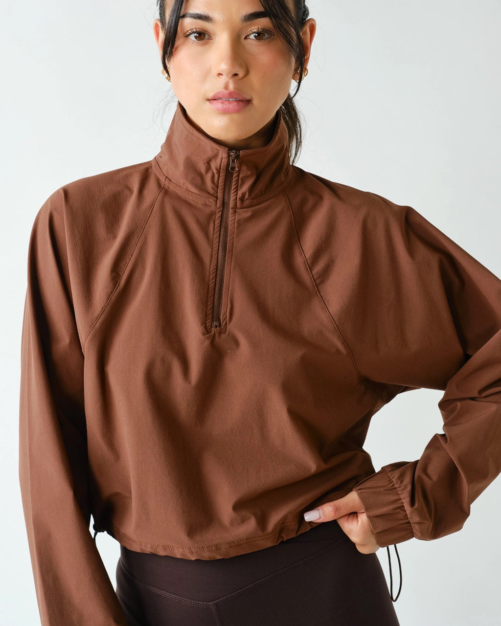 Women's chocolate brown half zip athleisure pullover with structured fit, long sleeves, four-way stretch fabric, and cropped silhouette.