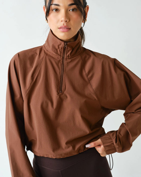 Women's chocolate brown half zip athleisure pullover with structured fit, long sleeves, four-way stretch fabric, and cropped silhouette.