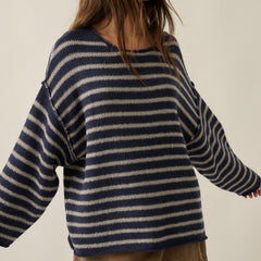 Woman wearing an oversized navy and oatmeal striped textured knit sweater with dropped shoulders and brown denim shorts.