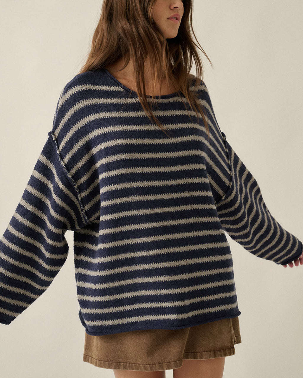 Woman wearing an oversized navy and oatmeal striped textured knit sweater with dropped shoulders and brown denim shorts.