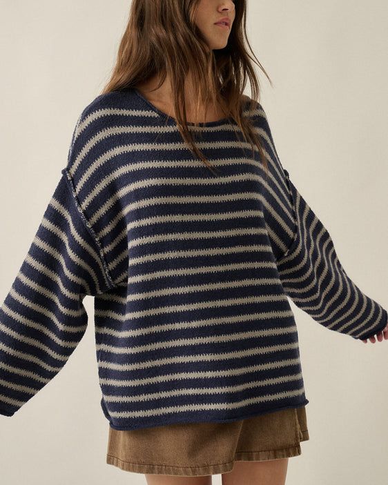 Woman wearing an oversized navy and oatmeal striped textured knit sweater with dropped shoulders and brown denim shorts.