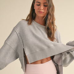 Women's gray oversized cropped waffle knit sweater with open sides styled with high-waisted blush leggings.
