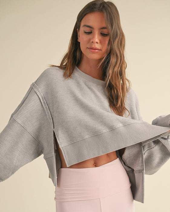 Women's gray oversized cropped waffle knit sweater with open sides styled with high-waisted blush leggings.